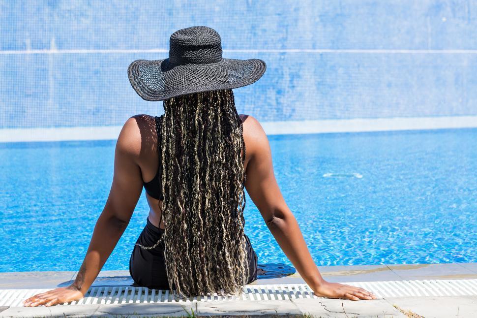 Free Image of Rear view of an African-American woman sitting on the edge of a pool 