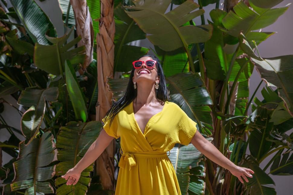 Free Image of Latina woman standing in a yellow dress and sunglasses 