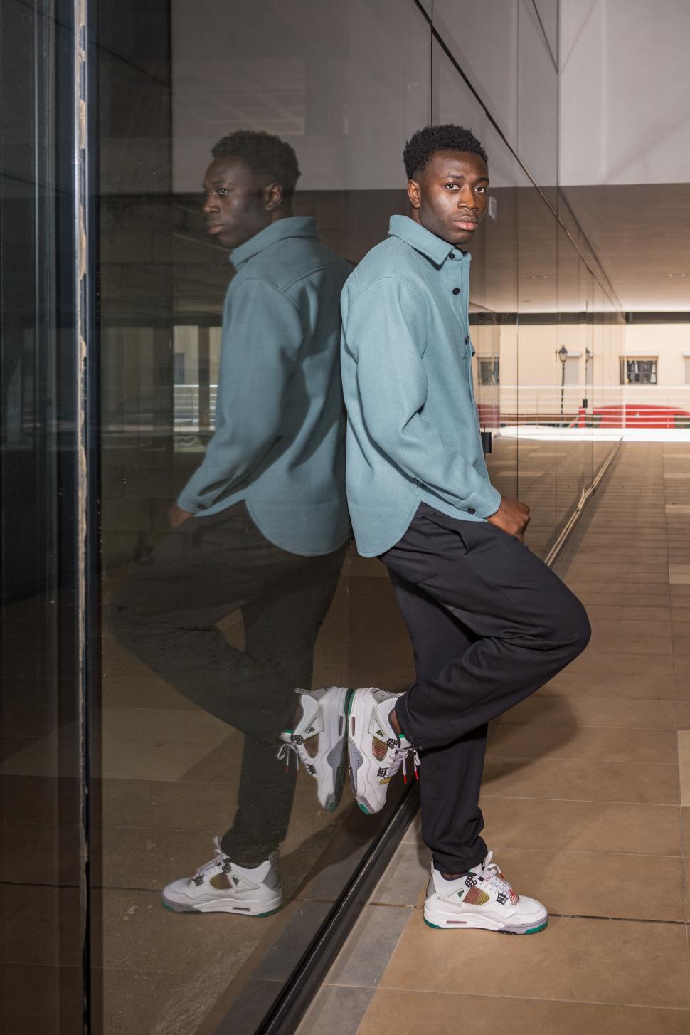Free Image of Fashionable young African American guy leaning on glass wall 