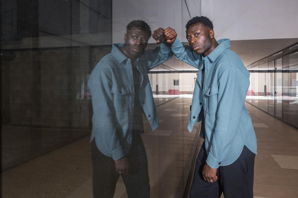 Free Image of Stylish African American guy leaning on reflecting glass wall 