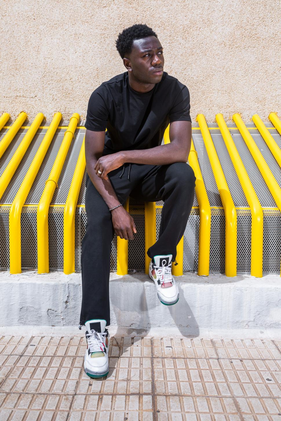 Free Image of Pensive trendy ethnic guy looking away while sitting on street 