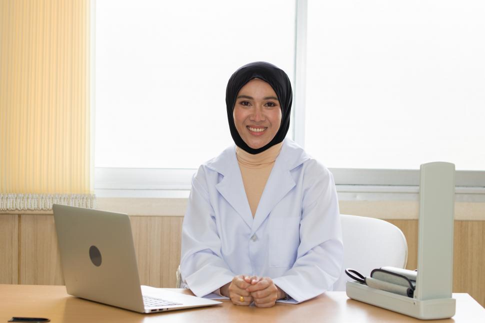 Free Image of Female doctor wearing a hijab sits at a table waiting for patient 