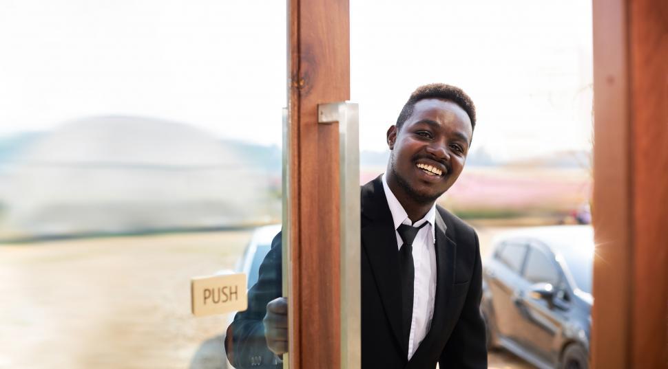 Free Image of Smiling man opening a large glass door. 