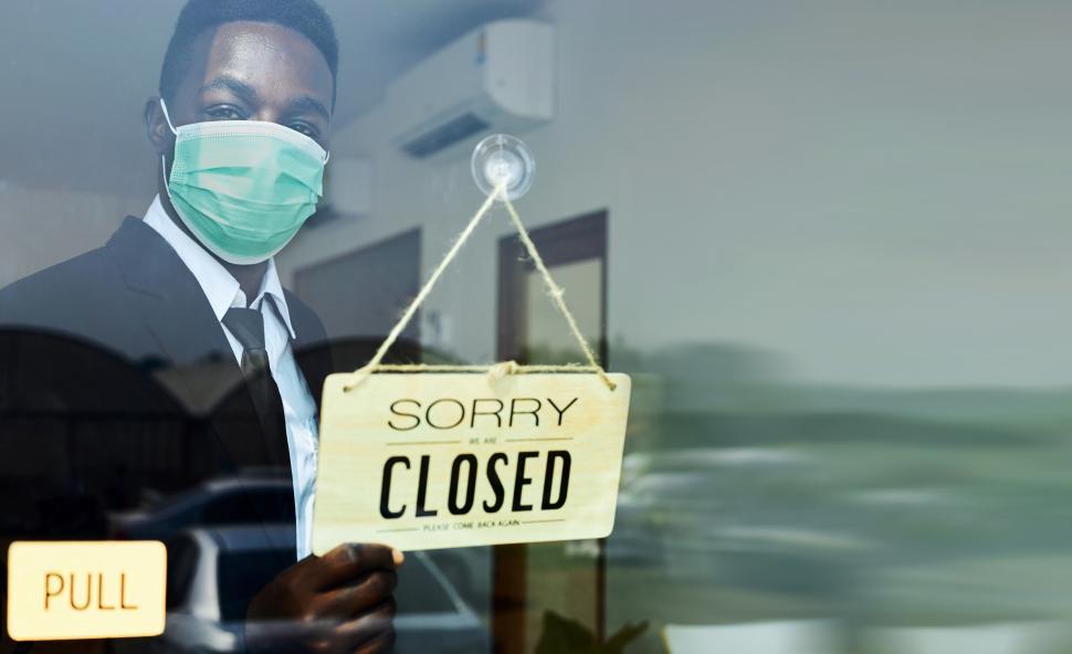 Free Image of Male waiter wearing an anti-virus mask flips sign to Closed 