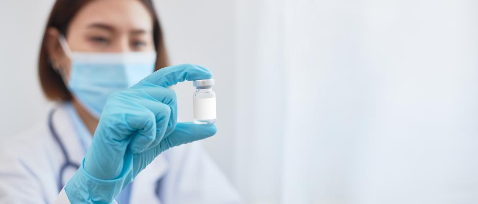 Free Image of A gloved doctor holding a vaccine bottle. 