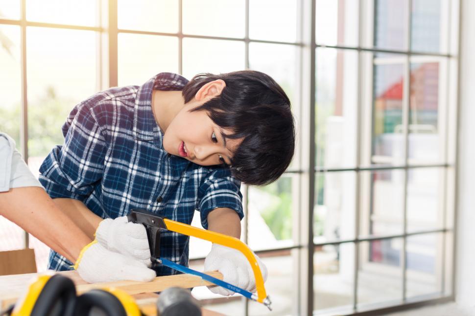 Free Image of Boy is trying to cut wood with a saw. 