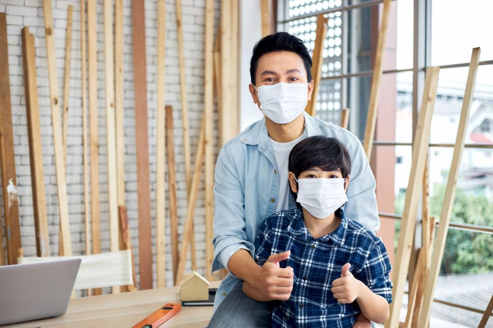 Free Image of Masked carpenter father sits with his son at his desk. 