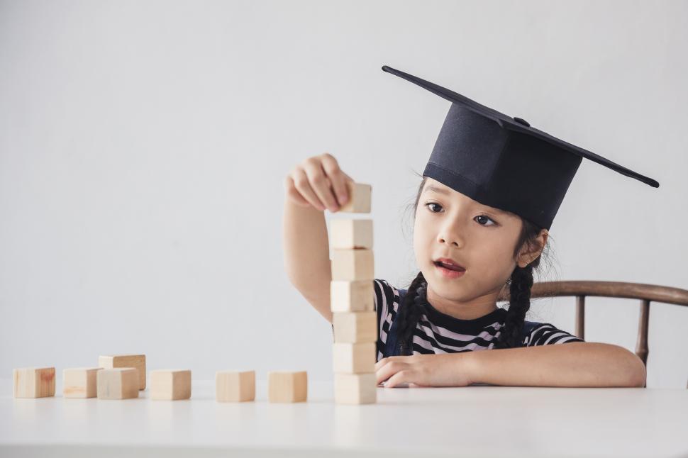 Free Image of Little girl wearing mortarboard stacking blocks 