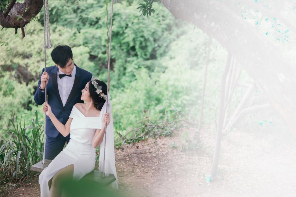 Free Image of Young bride sits on a swing alongside groom. With Copyspace 