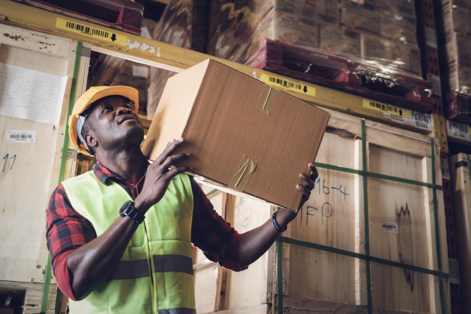 Free Image of Worker carrys heavy box on shoulder in the warehous 