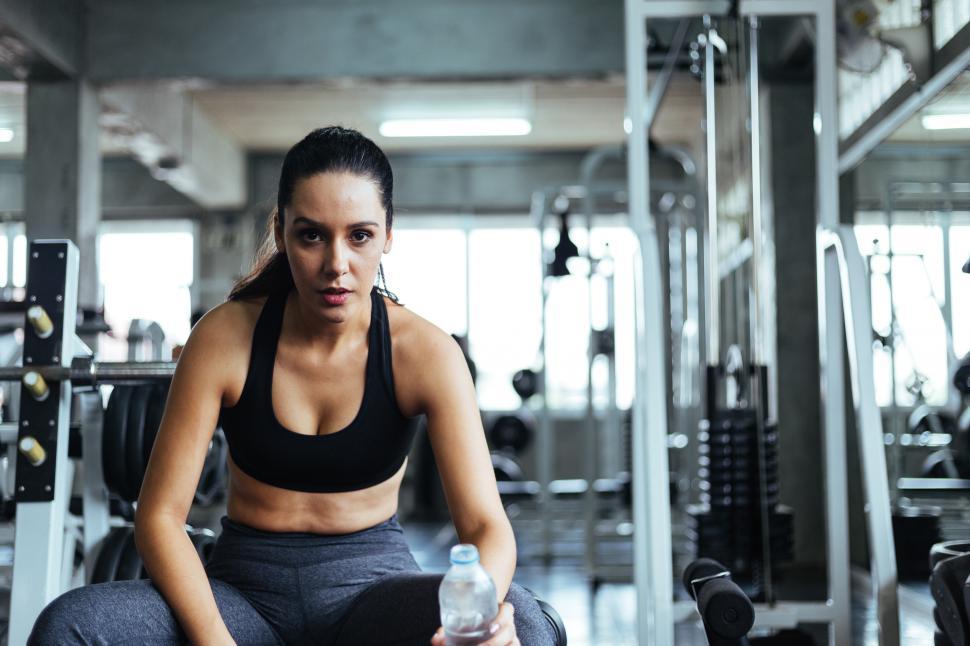 Free Image of Sporty woman in holding water bottle resting on gym bench 