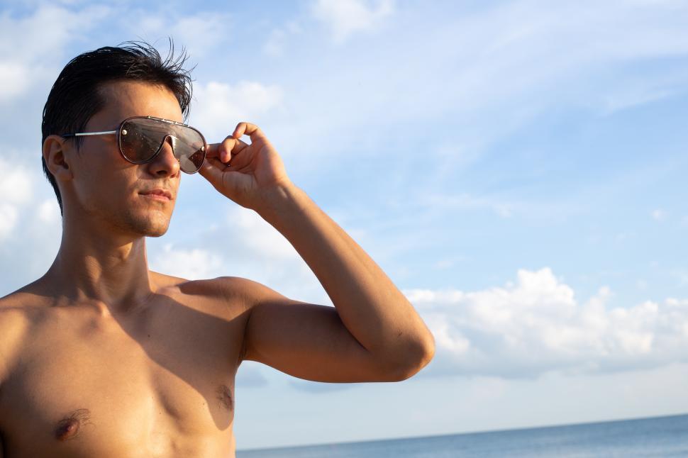 Free Image of Shirtless man wearing sunglasses standing at the beach 