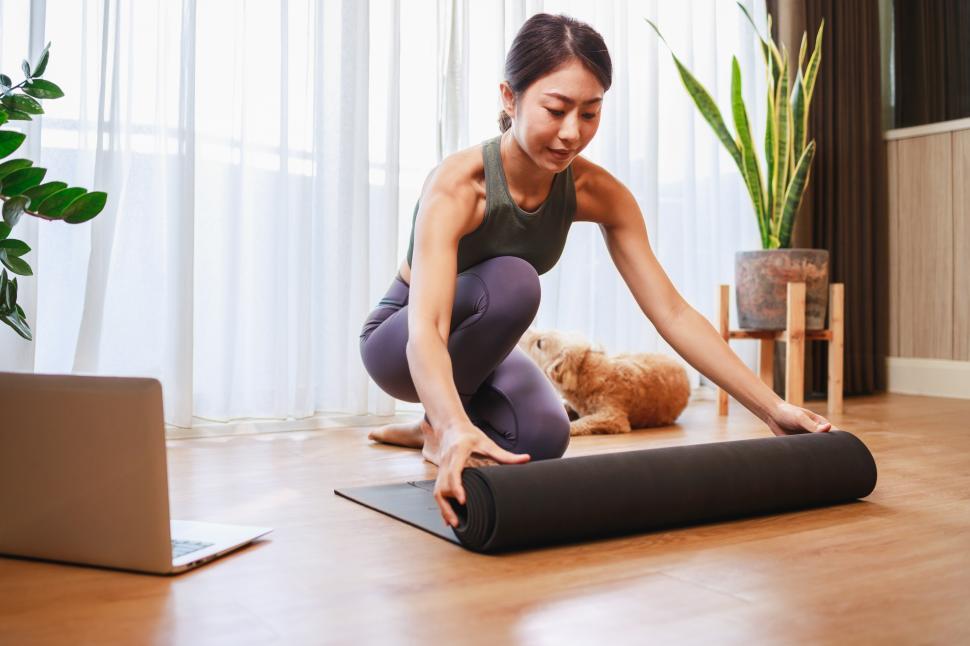 Free Image of Young woman unrolling roll black yoga mat for online training 