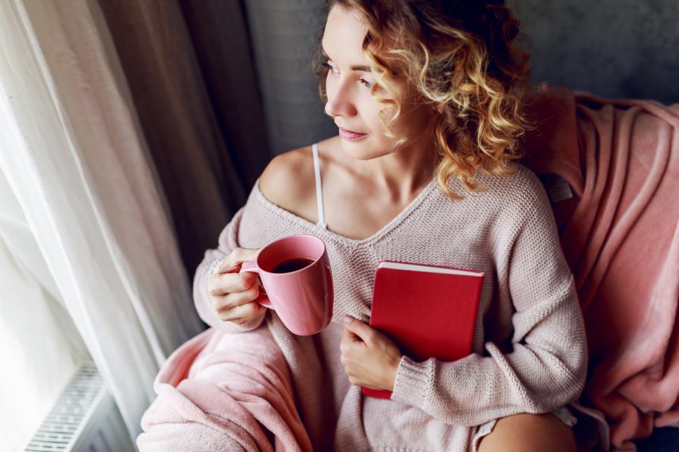 Free Image of Pensive blonde woman relaxing on couch at home with hot beverage 