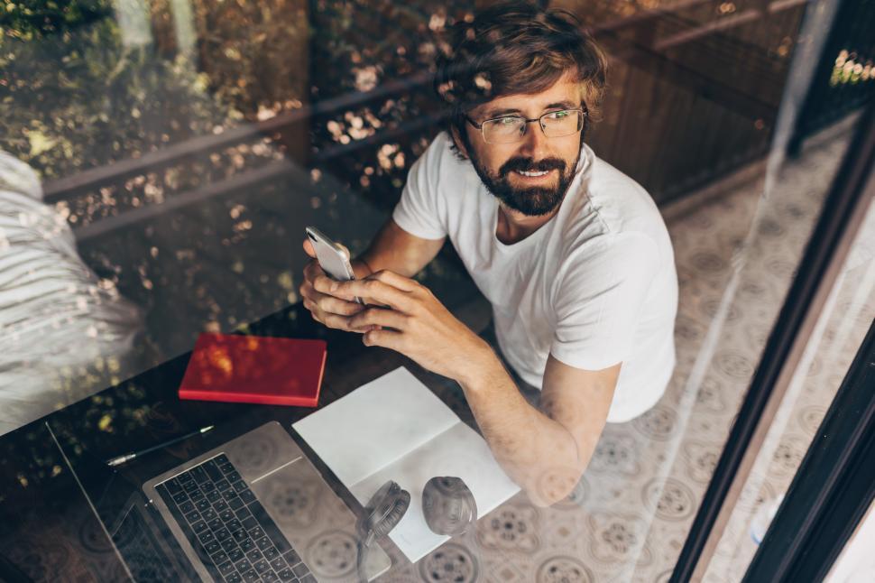 Free Image of Happy man using smartphone and looking through the window 