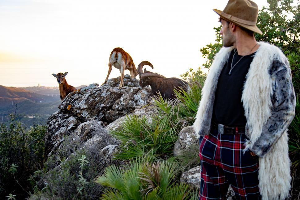 Free Image of a man in the mountains with goats at the back 