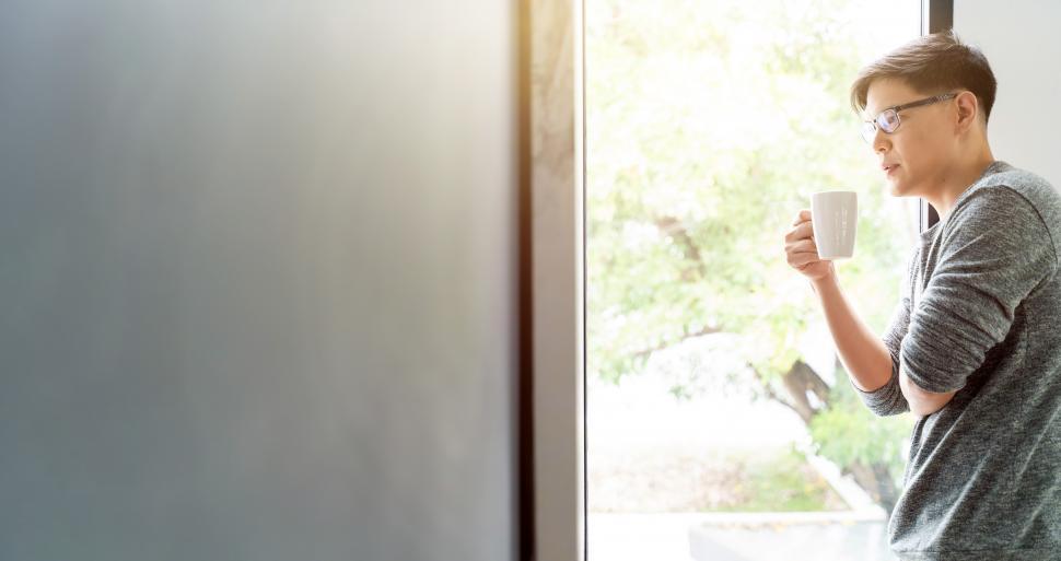 Free Image of Young man drinking hot coffee while looking through window 