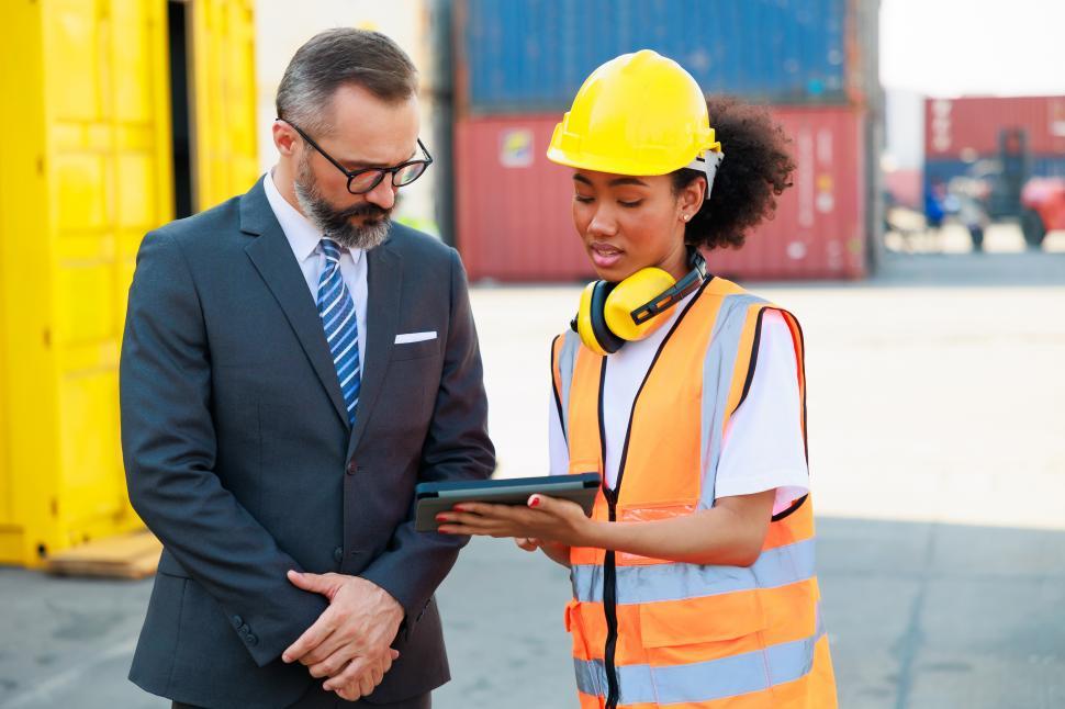 Free Image of Caucasian business man and black female dock worker look at tablet device 