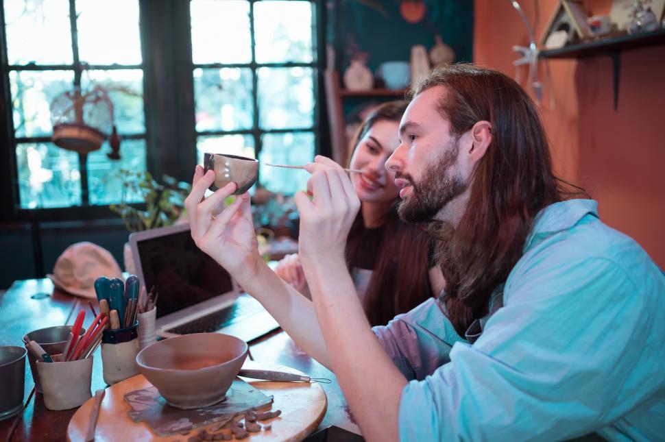 Free Image of Young couple in the pottery shop they own, looking at a small pot 