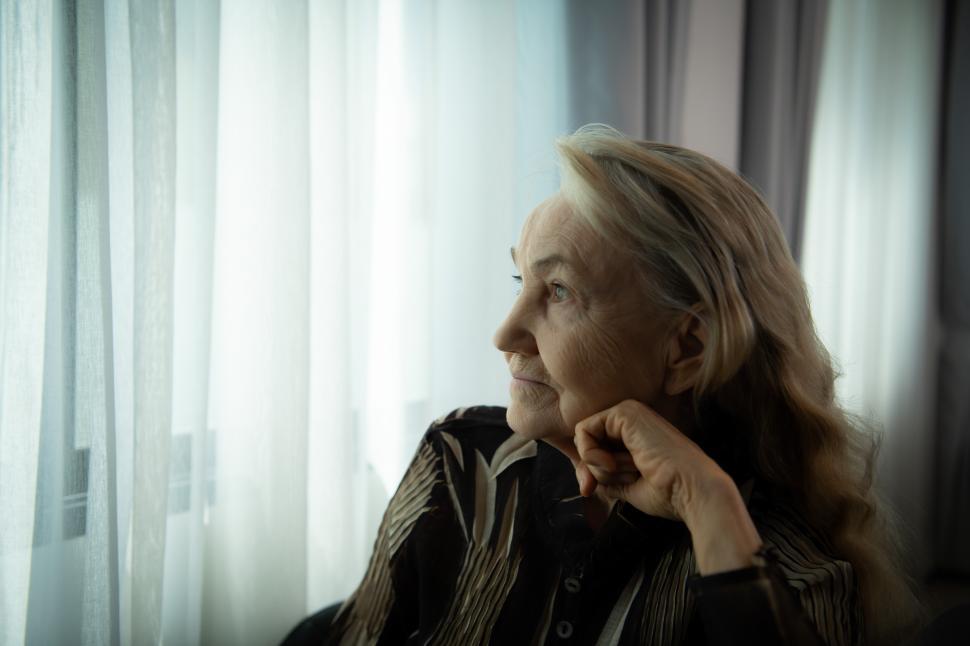 Free Image of Lonely old woman Sits by herself and looks out the window 