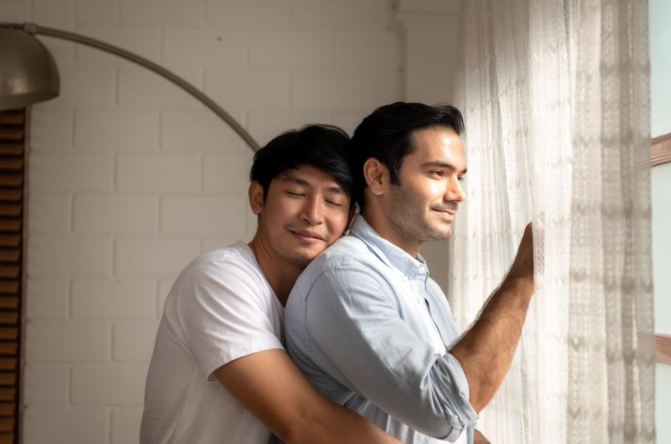 Free Image of Happy man looks out the window while being embrace by his partner 