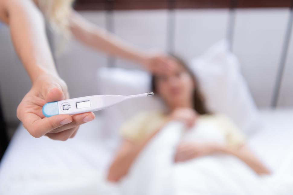 Free Image of Close up of a thermometer with a sick person in the background 