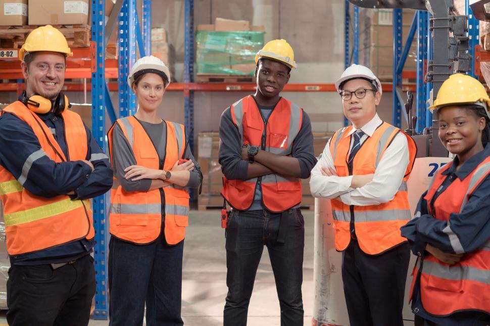 Free Image of Portrait of a group of employees in a warehouse, arms crossed, in safety gear 