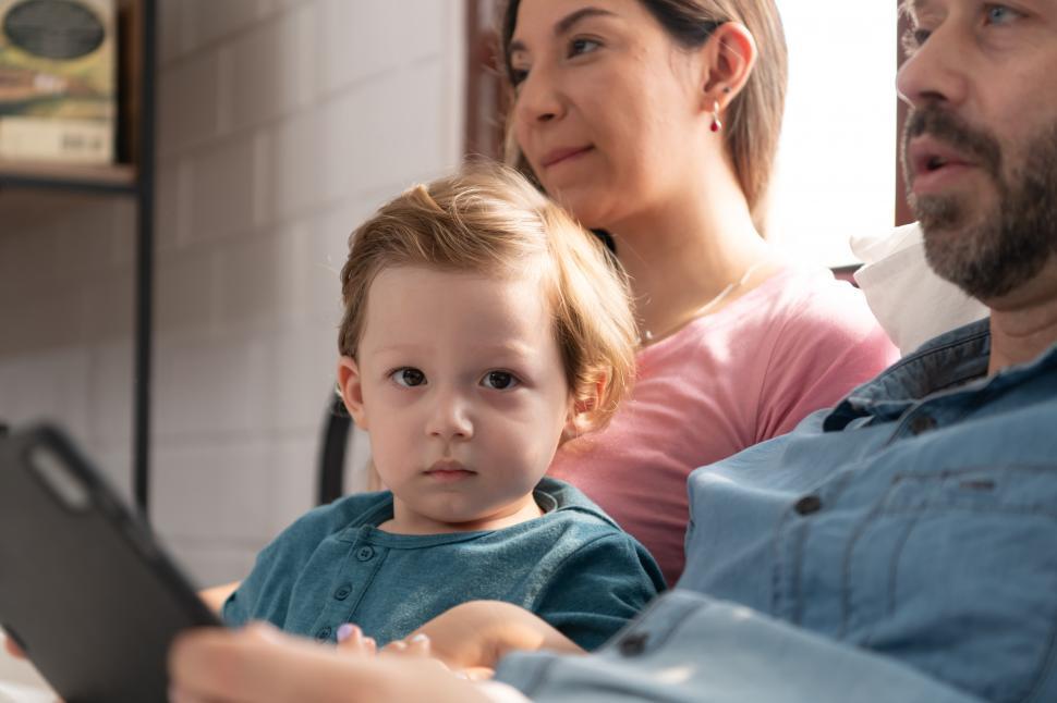 Free Image of Little boy sitting in the lap of his parents, looking at the camera 