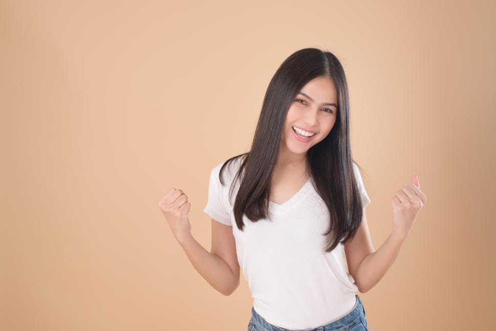Free Image of Woman wearing white T-shirt makes fists over brown backgroud 