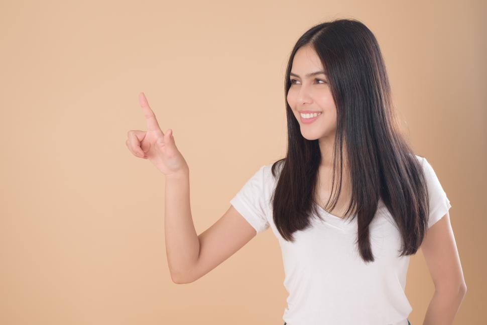 Free Image of Woman points in space at item to be added. Brown background with copyspace 