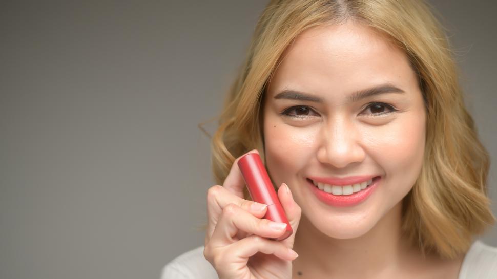Free Image of Young blonde woman holding cosmetic products for camera 
