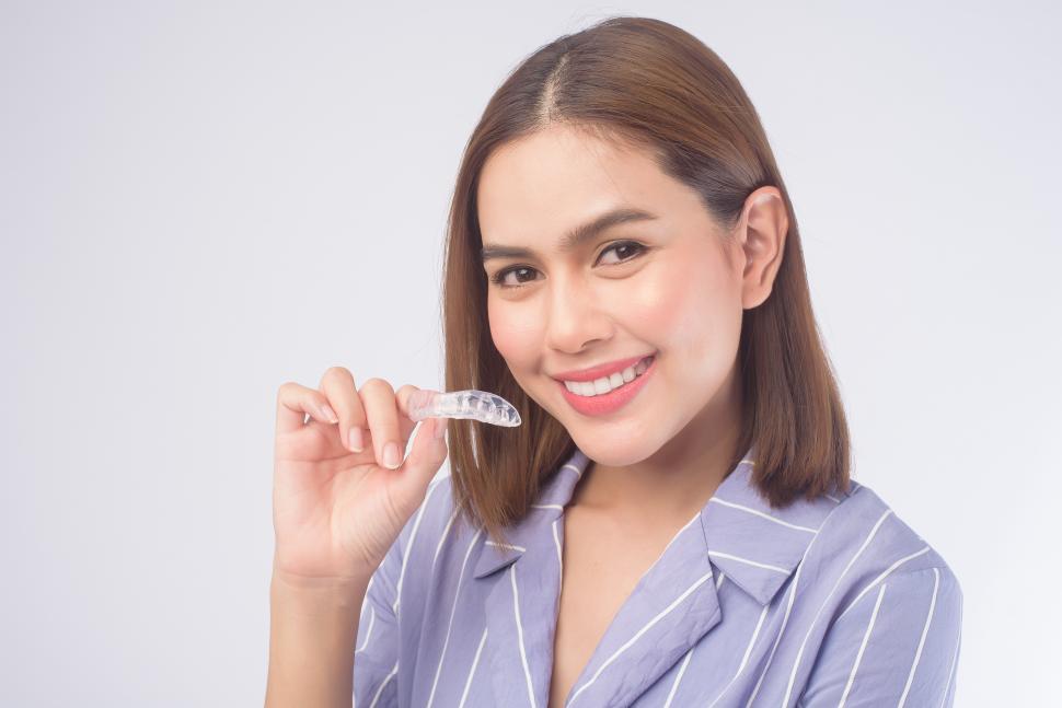 Free Image of Young smiling woman holding clear plastic braces over white background 