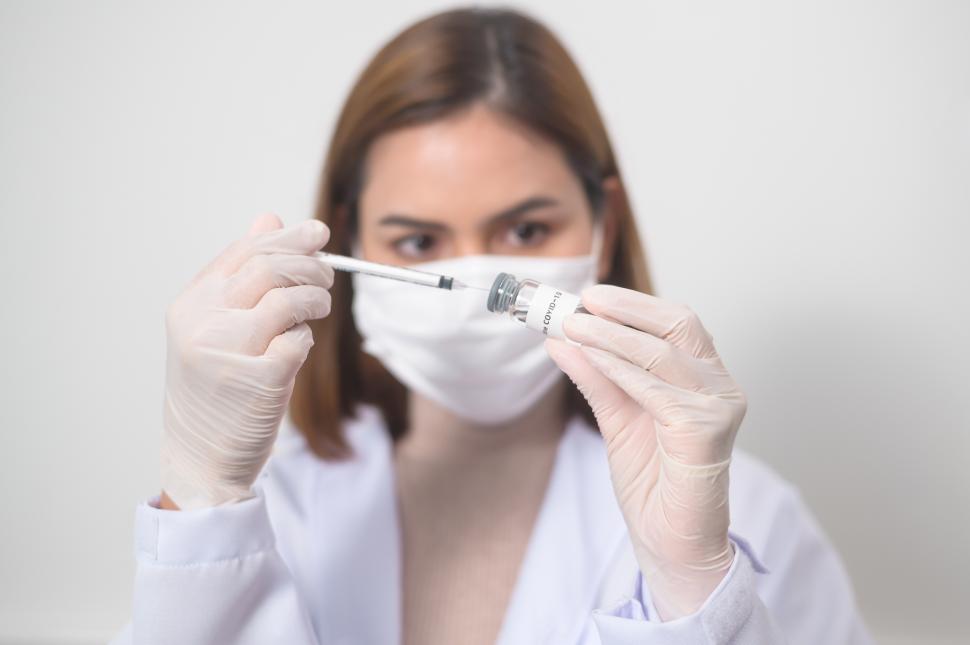 Free Image of Young female doctor extracting a dose with syringe from covid-19 vaccine bottle 