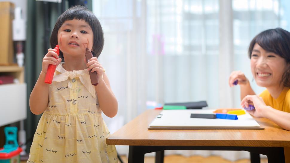 Free Image of Young mom helping daughter draw with colored pencils in living room 