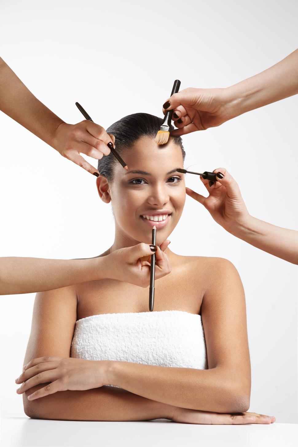 Free Image of Woman sitting while many hands come in to apply makeup 
