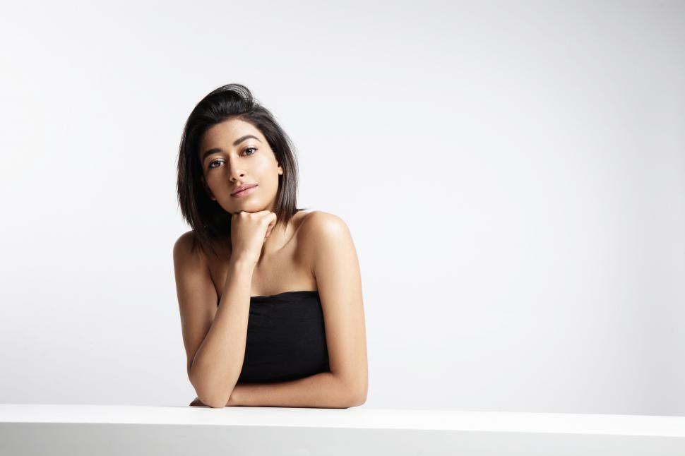 Free Image of Attractive young woman in white studio space, chin on hand 