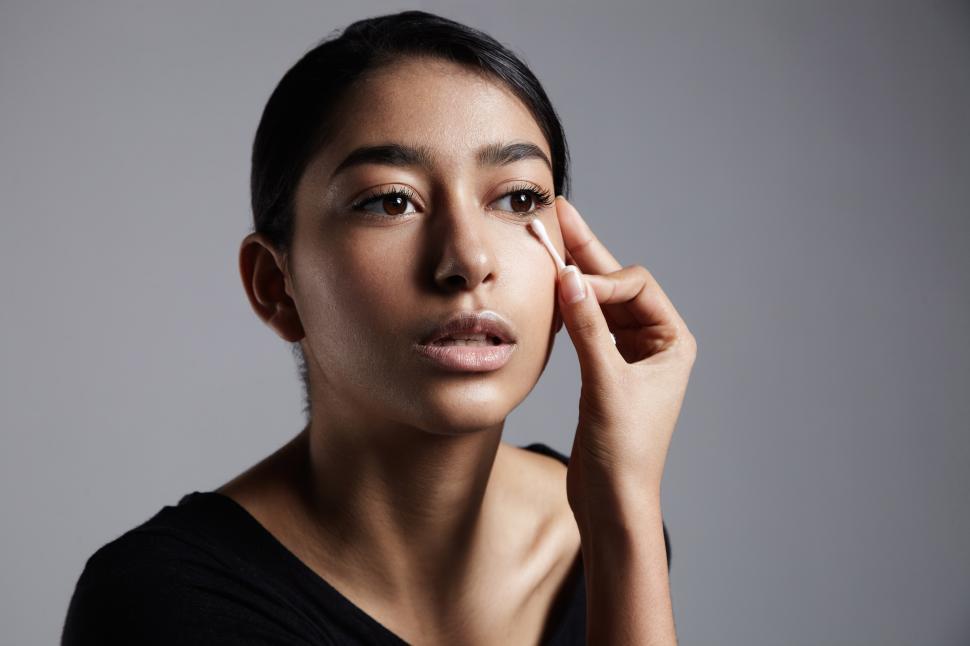Free Image of Young woman correcting a makeup flaw with cotton swab 