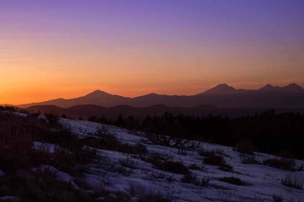 Free Image of A snowy mountain with trees and mountains in the background 