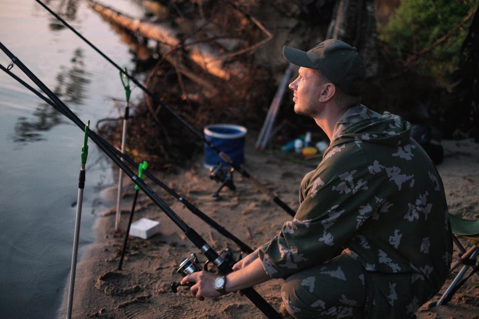 Free Image of A man sitting on the beach holding fishing poles 