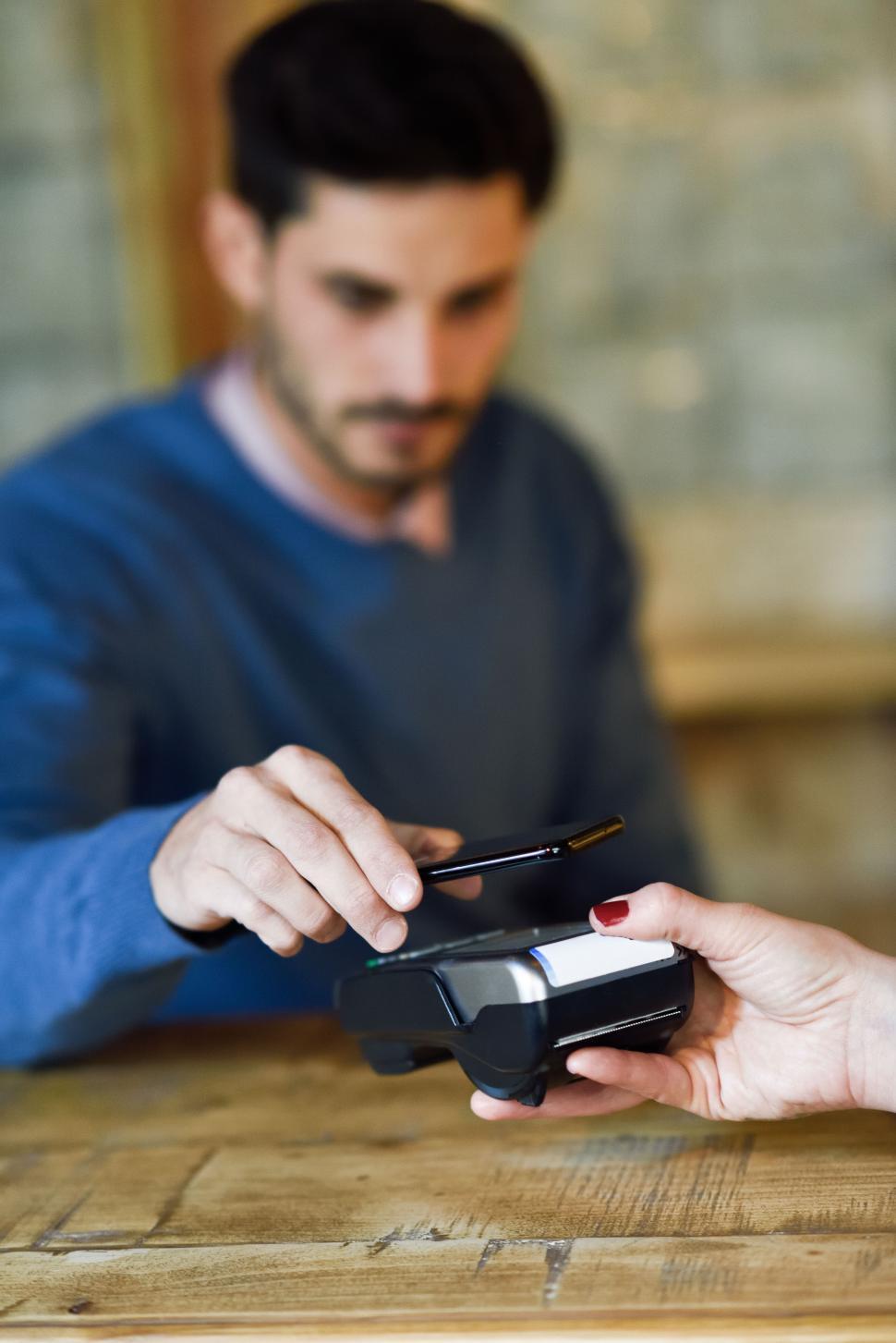 Free Image of Hand holding smartphone paying on EDC machine. 