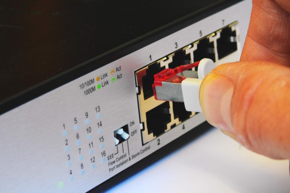 Free Image of A hand connecting a red and white cable to a network port 