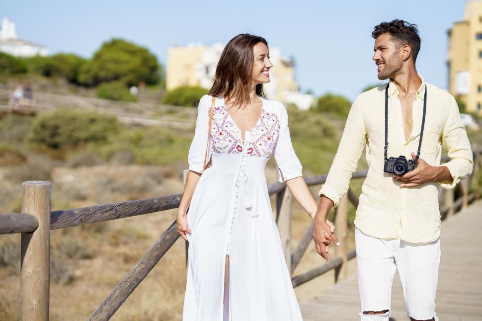 Free Image of Loving couple walking along a wooden path towards the beach in a coastal area. 