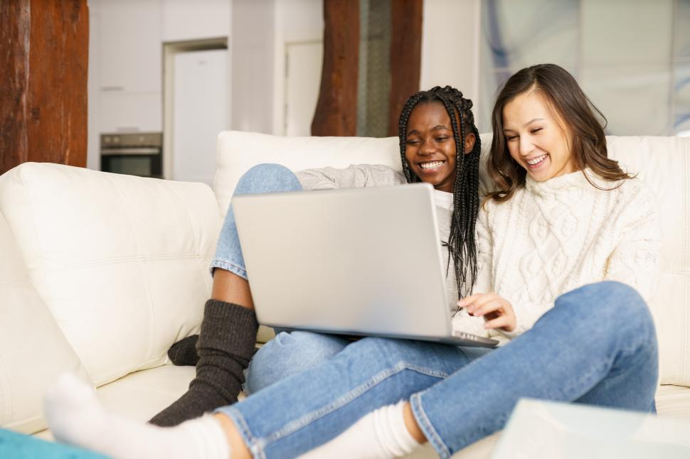 Free Image of Two female student friends sitting on the couch at home using a laptop. 