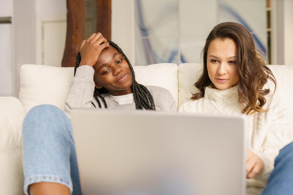 Free Image of Two female student friends sitting on the couch at home using a laptop. 