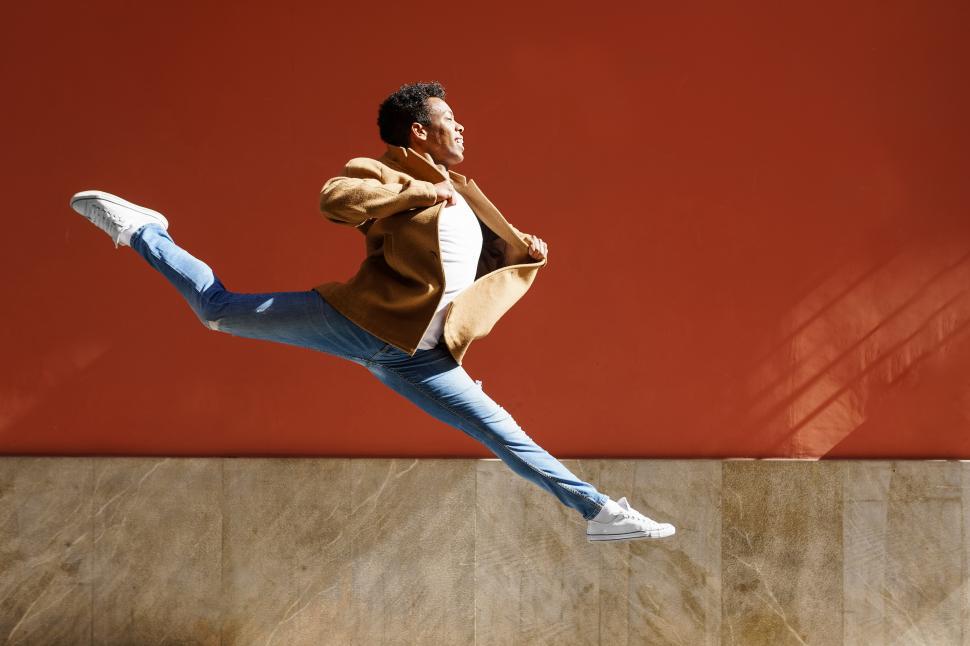 Free Image of Happy black guy doing an acrobatic jump in the middle of the street. 