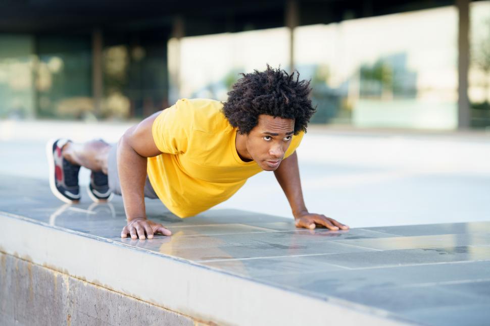 Free Image of Black man doing pushups on city street bench. 