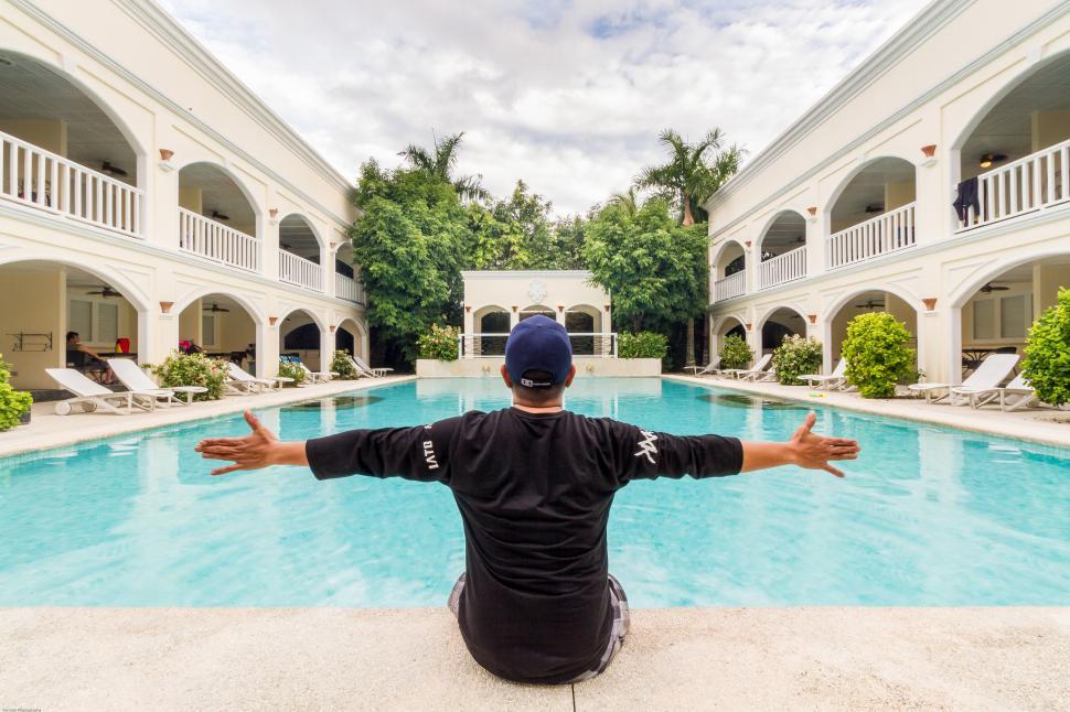 Free Image of A man sitting on the edge of a pool with his arms outstretched 