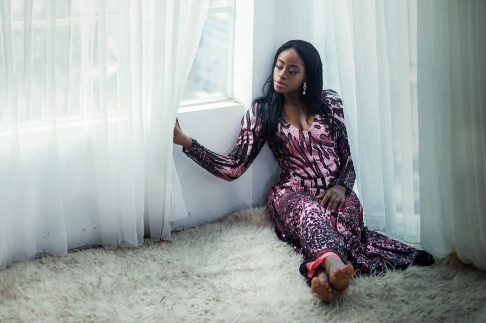 Free Image of A woman sitting on the floor looking out a window 