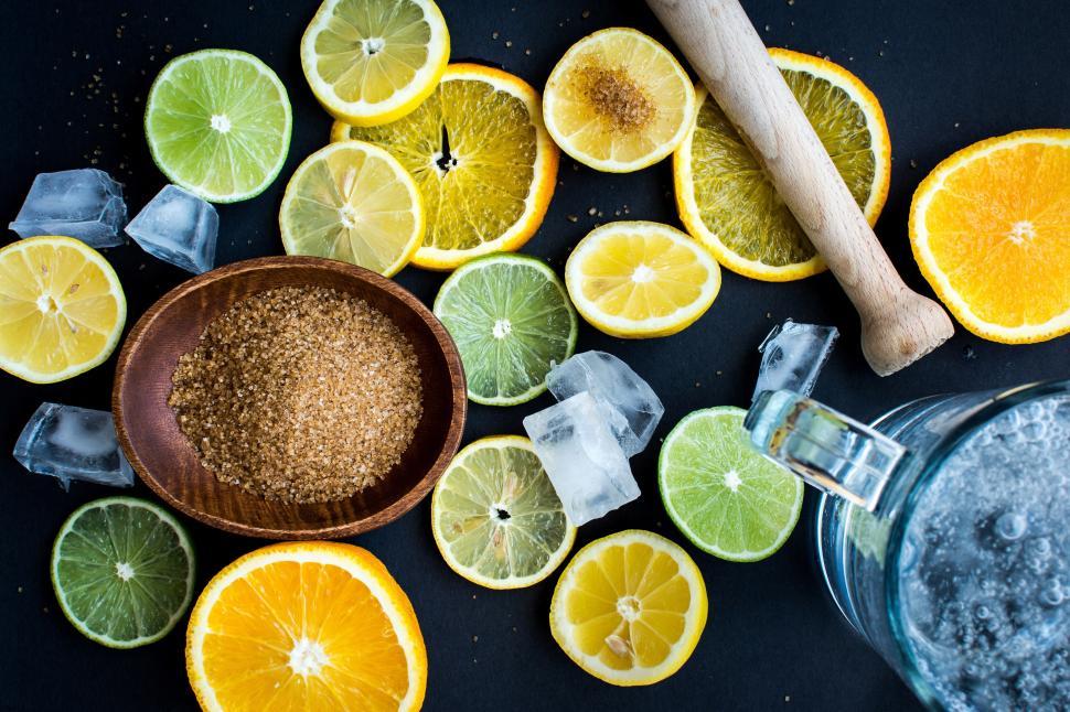 Free Image of A group of sliced lemons and limes with a wooden bowl of brown sugar and a glass pitcher of water 