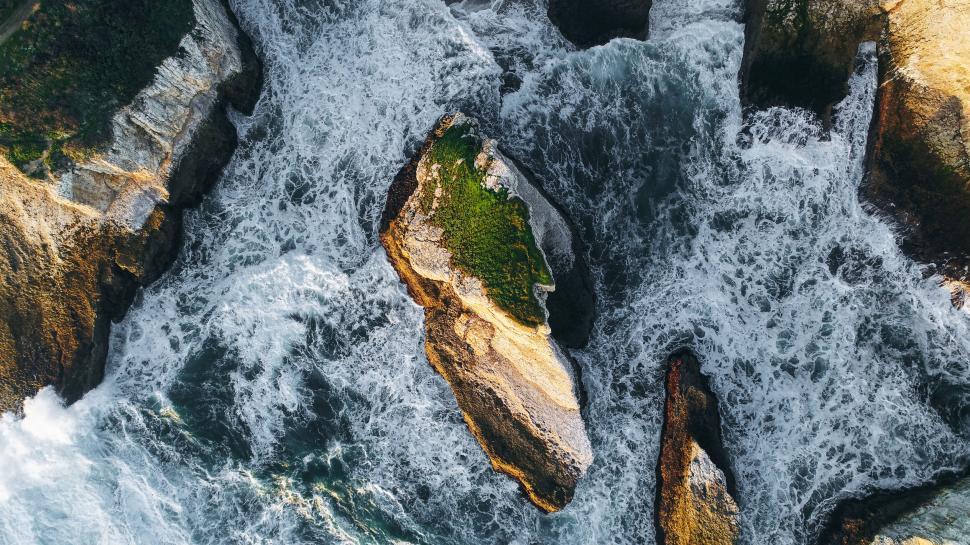Free Image of A rock with a green patch on it surrounded by waves 
